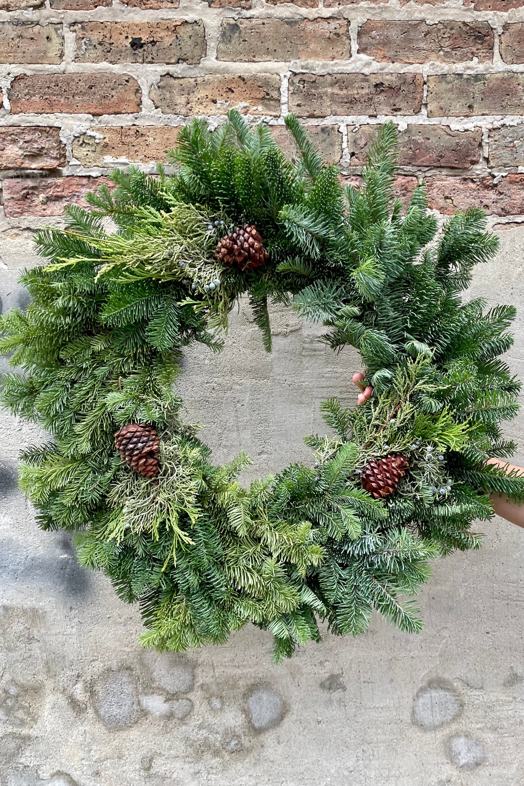 A mixed noble wreath 24" round begins held against a brick and concrete wall. ©Sprout Home
