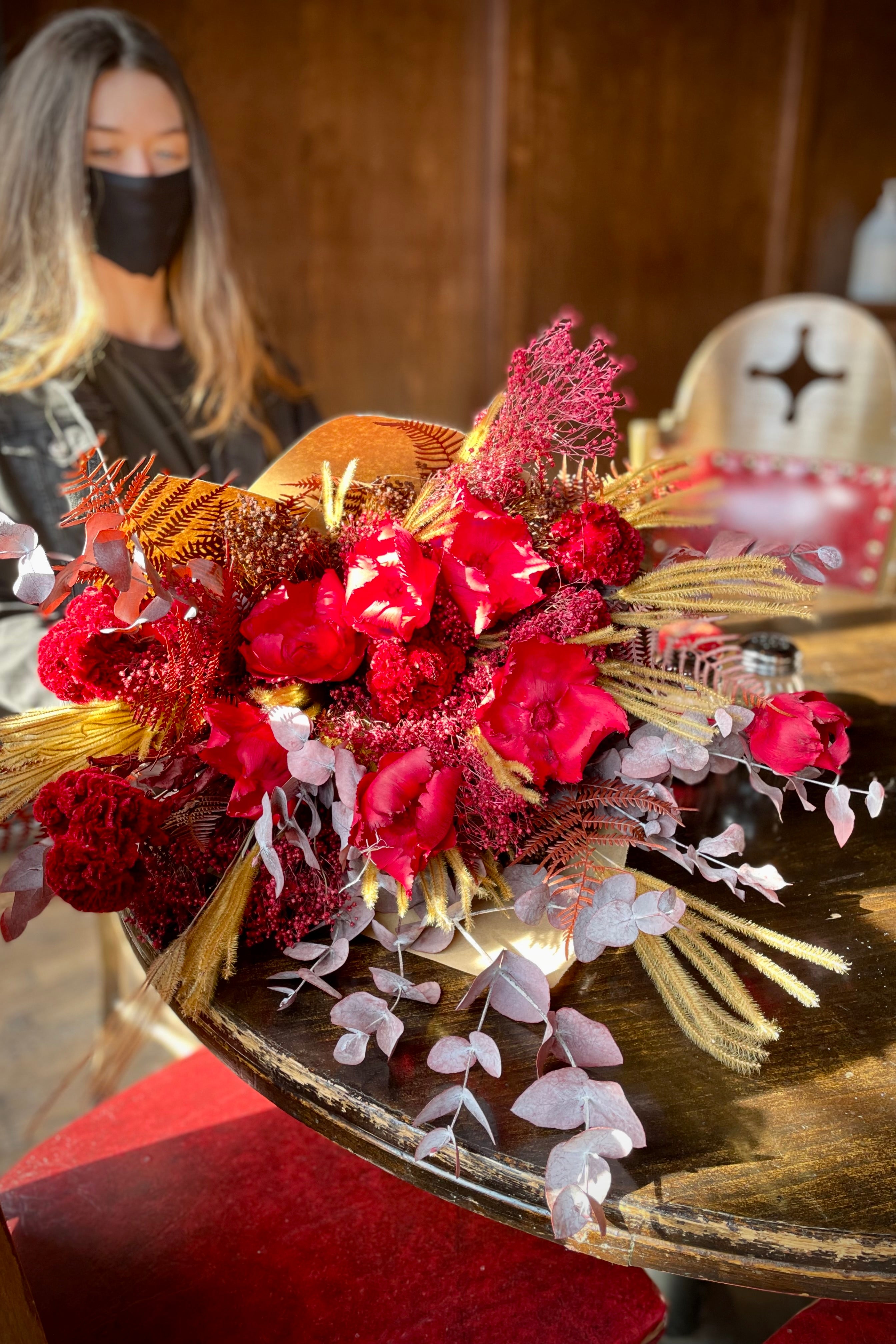 Preserved Red Velvet arrangement laying on a table with our floral designer sitting. #size_$200