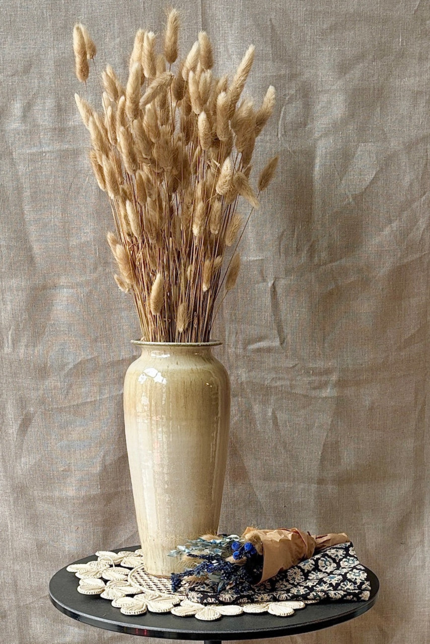 Beige vase with dried Lagurus in natural color on a textured surface against a beige wall ©Sprout Home