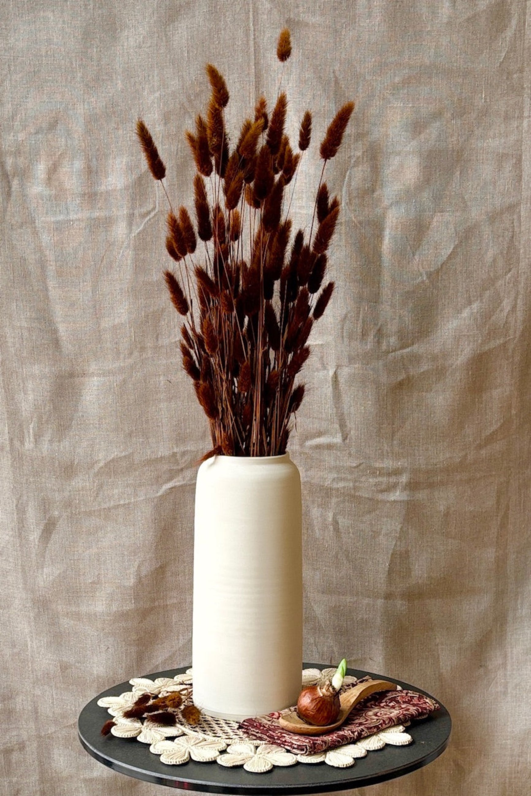 White vase with dried Lagurus in warm brown on a decorative tray against a textured beige background ©Sprout Home