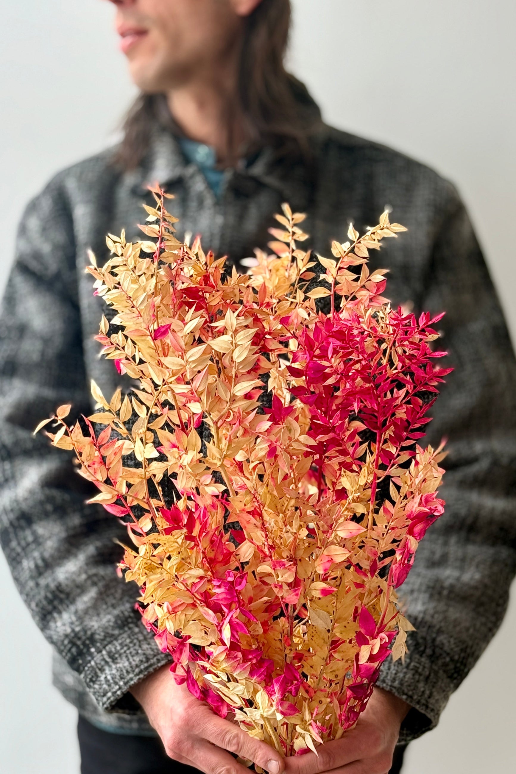 Person holding a bouquet of pink and tan ruscus preserved leaves against a neutral background ©Sprout Home