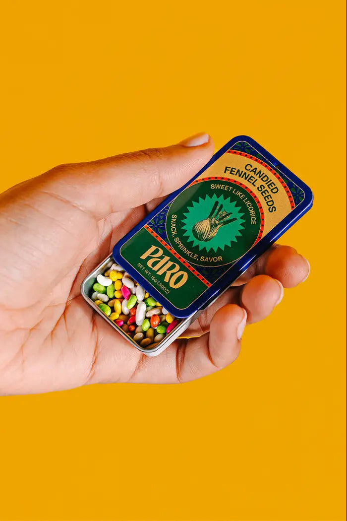 Candied Fennel Seeds in its tin being held in hand against a orange wall ©Paro