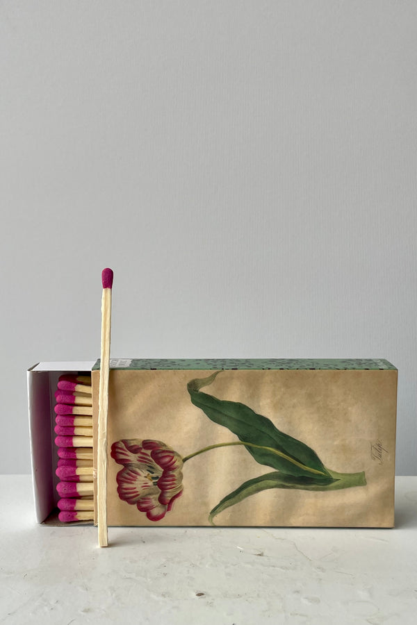 Photo of a tulip matchbox and matches against a white wall.