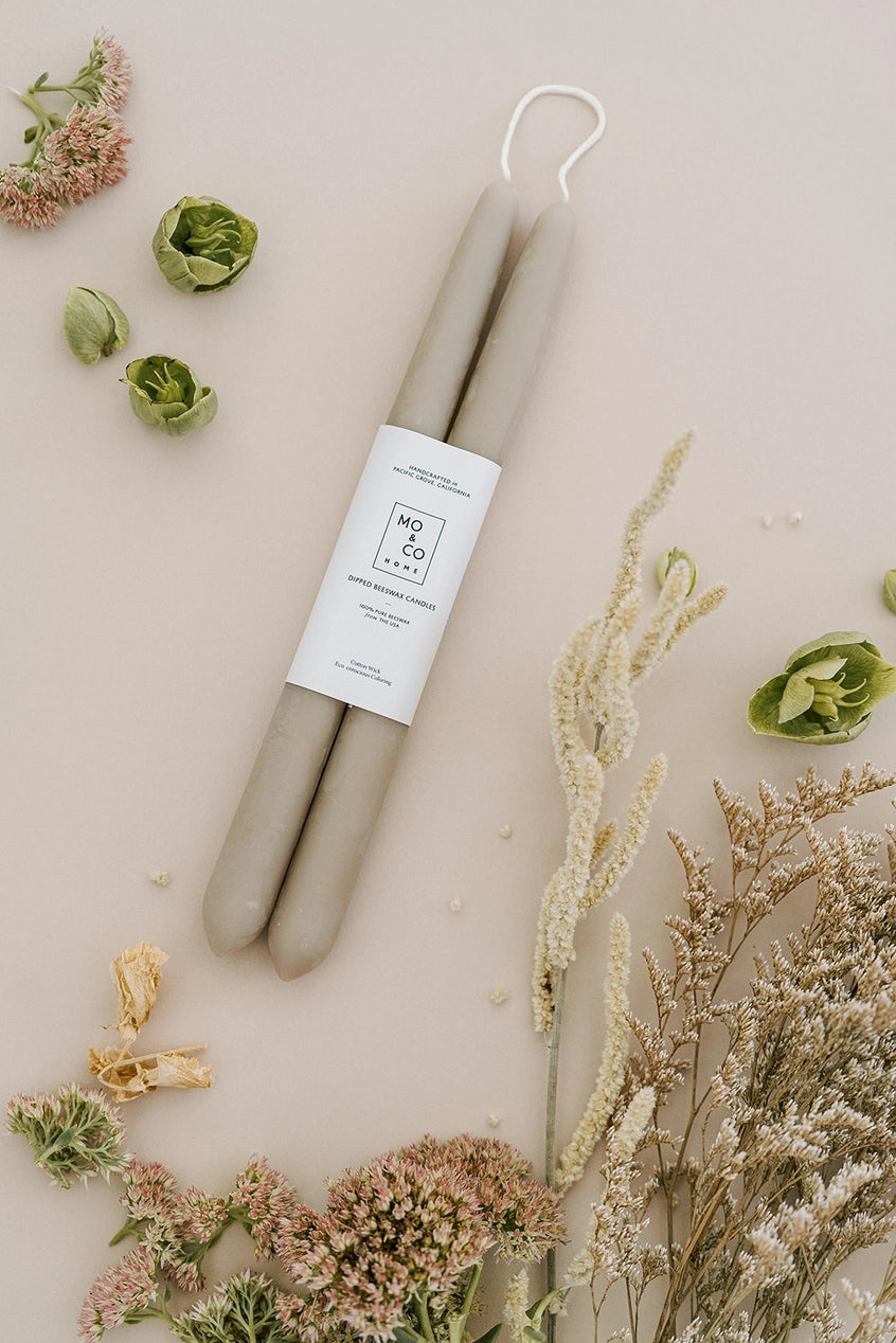 Mo & Co Clay beeswax candles pair laying flat with natural soft colored botanicals lying near them.