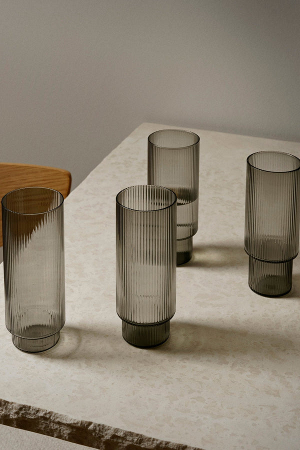 Set of four smoked tall ripple glass by Ferm Living sitting on a marble table in a room.