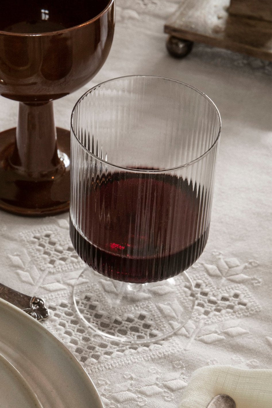 One Clear Ripple wine glass by Ferm Living with red wine inside on a white lace tablecloth.