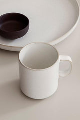 The Cream colored Sekki Mug in front of a Sekki plate by Ferm Living.