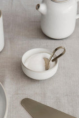 Sekki cream salt jar by Ferm Living filled with salt and a brass spoon in a lifestyle shot. 