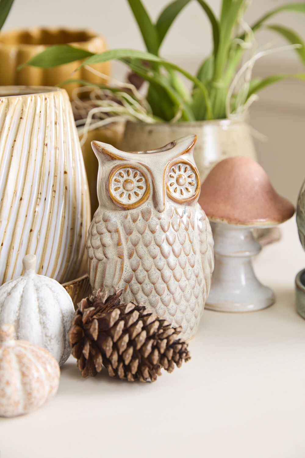 Decorative owl figurine with a pine cone and small pumpkins on a surface. ©Accent Decor