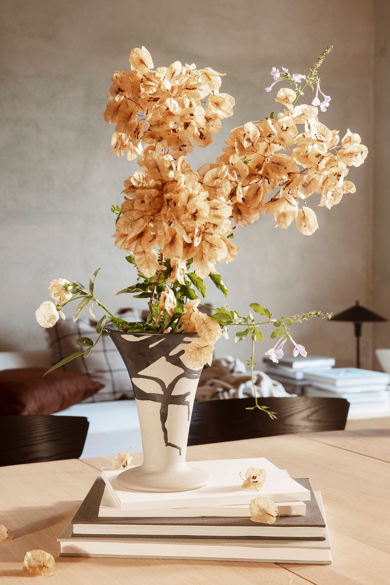 The Flores vase with cream colored floral inside and sitting on a stack of books in a living room.