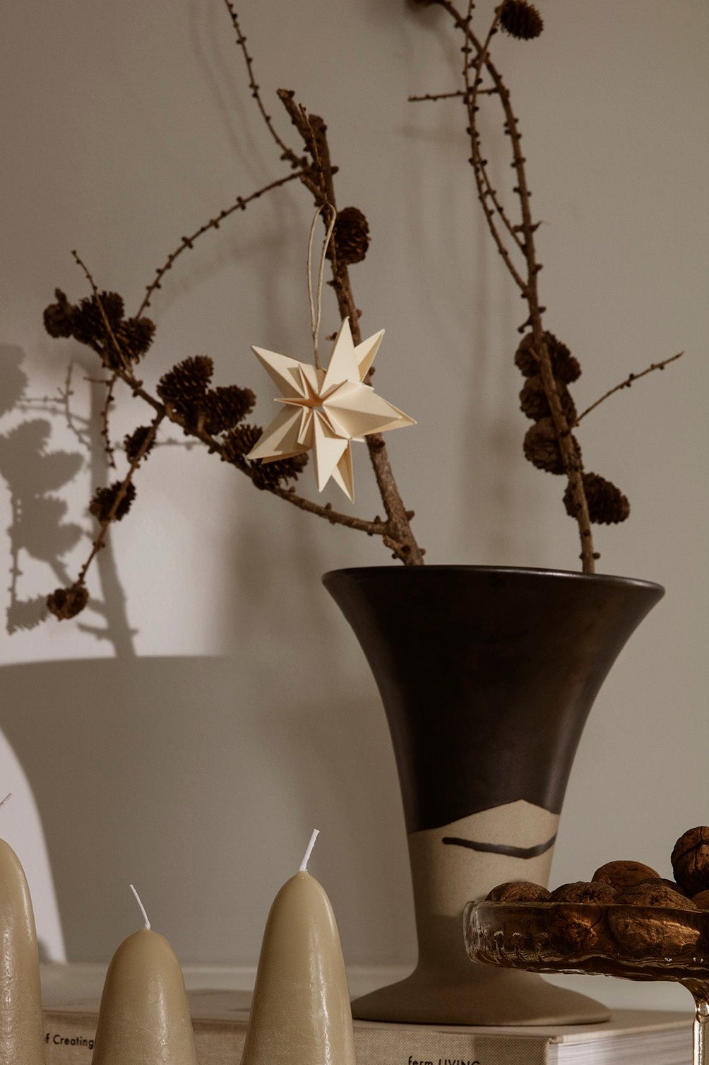 The Flores vase with dried branches and a hanging white paper star in a dimly lit room. 