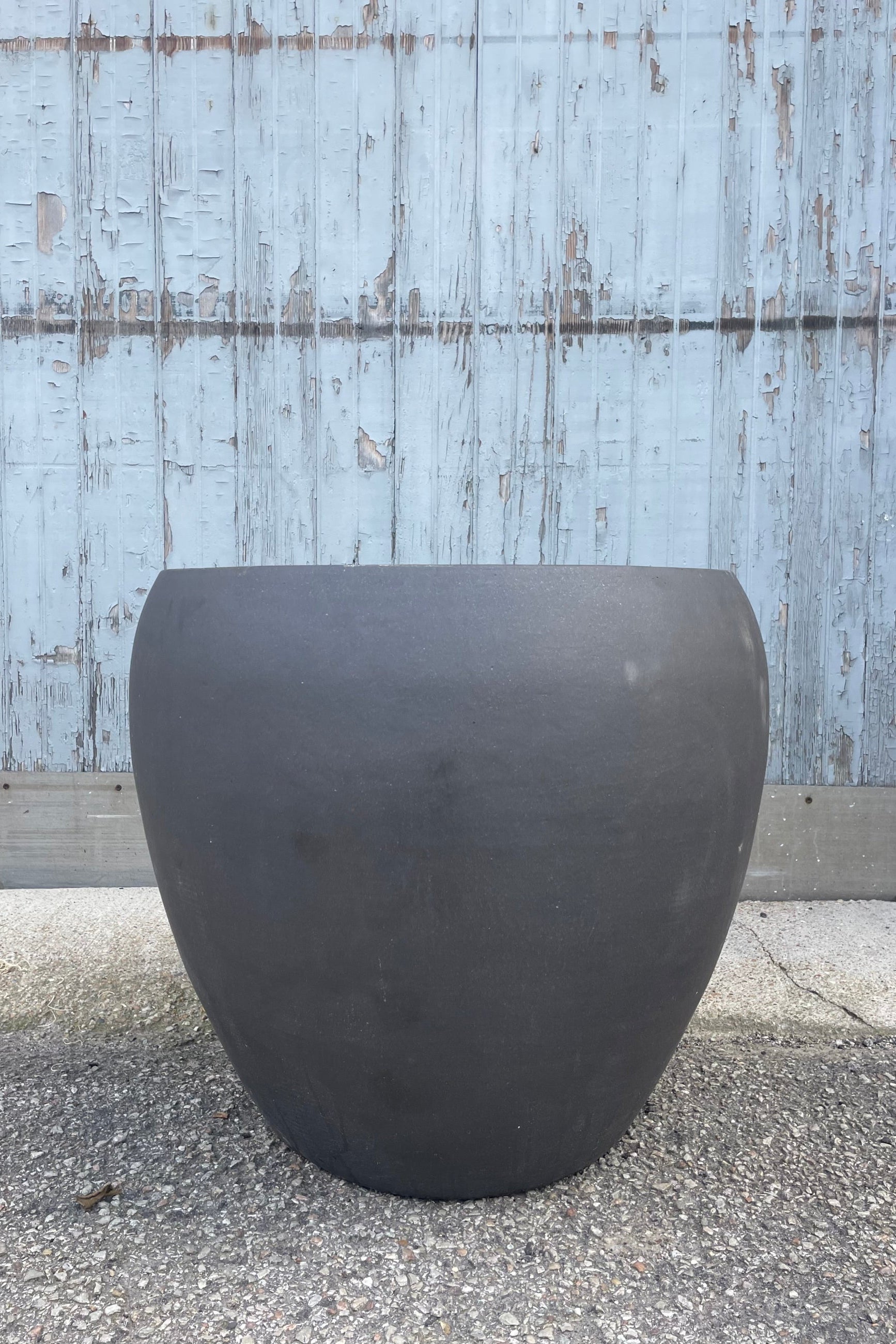 Photo of a rounded brown planter on a gravel surface in front of a textured wall ©Sprout Home