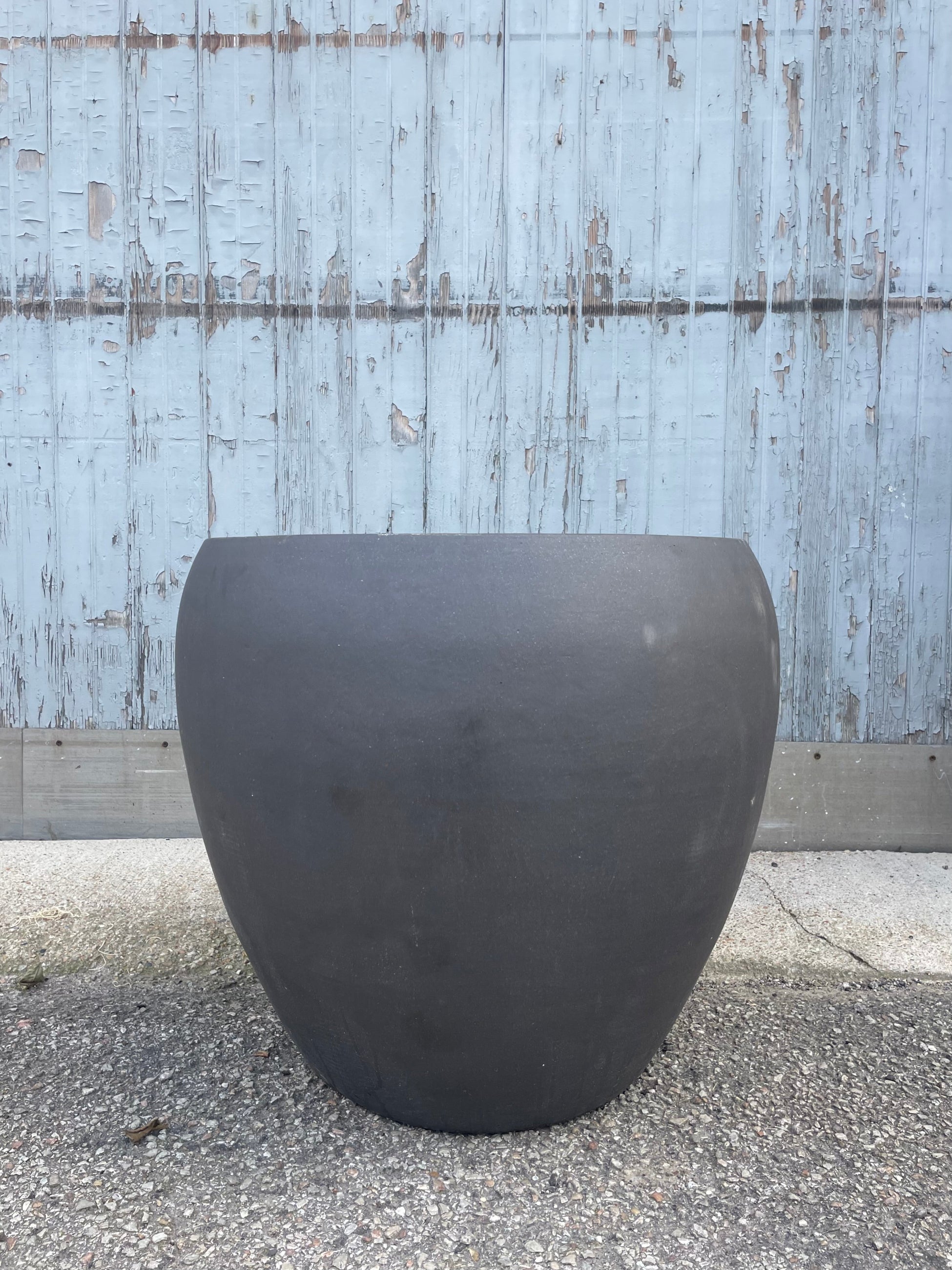 Photo of a rounded brown planter on a gravel surface in front of a textured wall ©Sprout Home