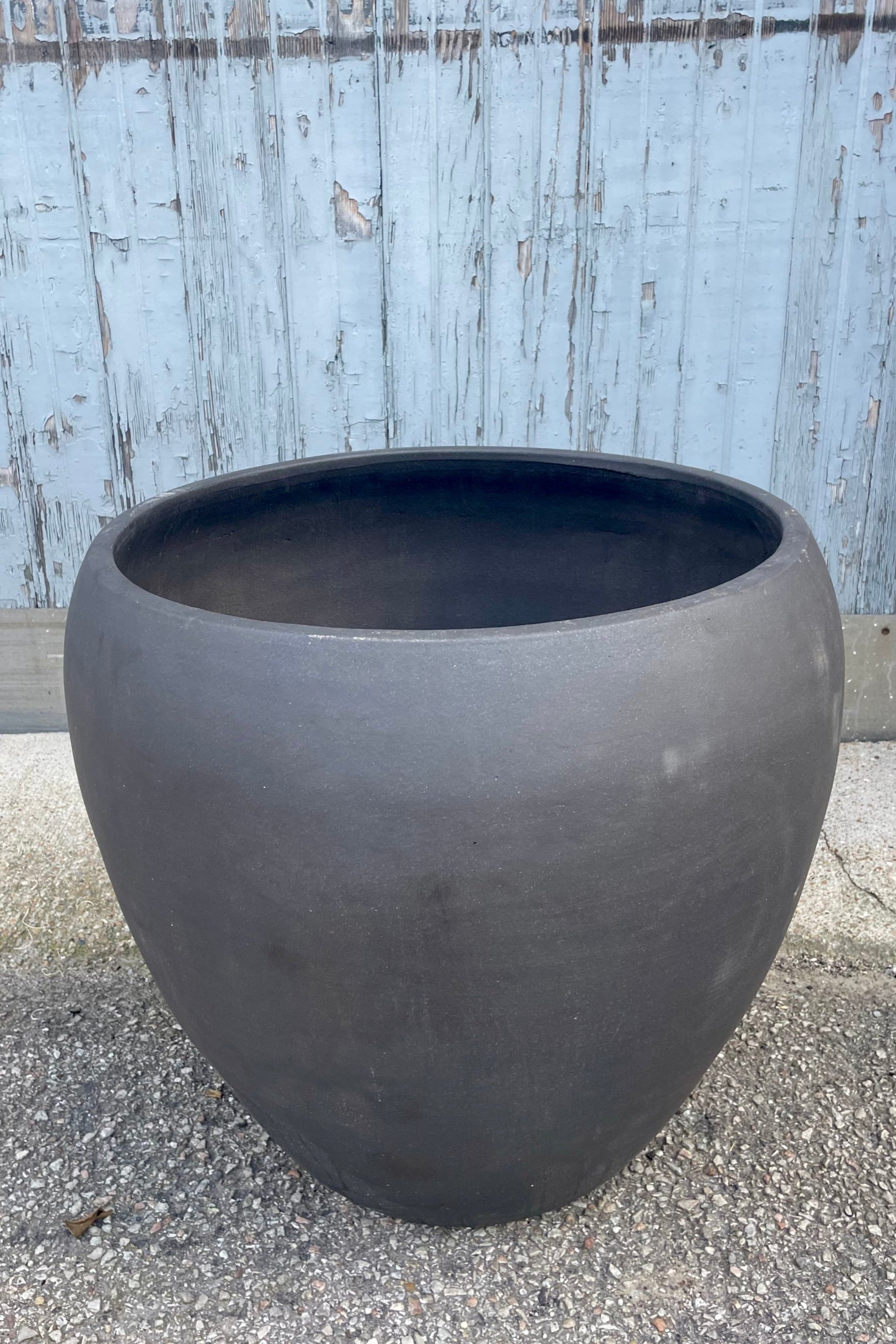 Photo of a rounded brown planter on a gravel surface in front of a textured wall ©Sprout Home