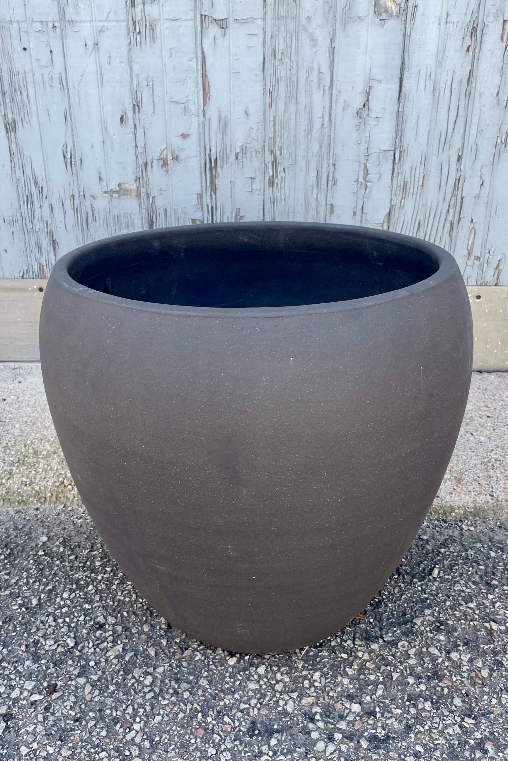 Photo of a rounded brown planter on a gravel surface in front of a textured wall ©Sprout Home