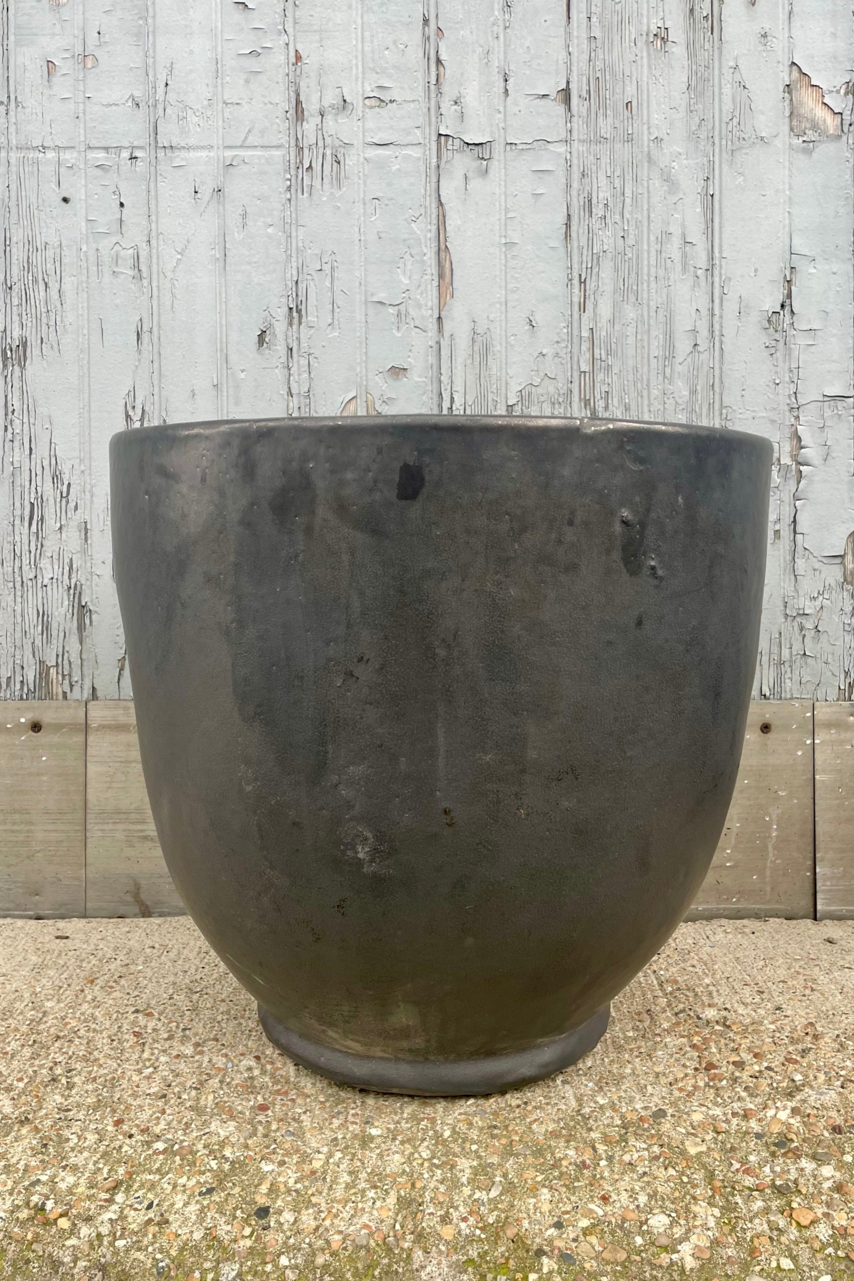 A dark gray planter in front of a wooden wall. Front view. ©Sprout Home