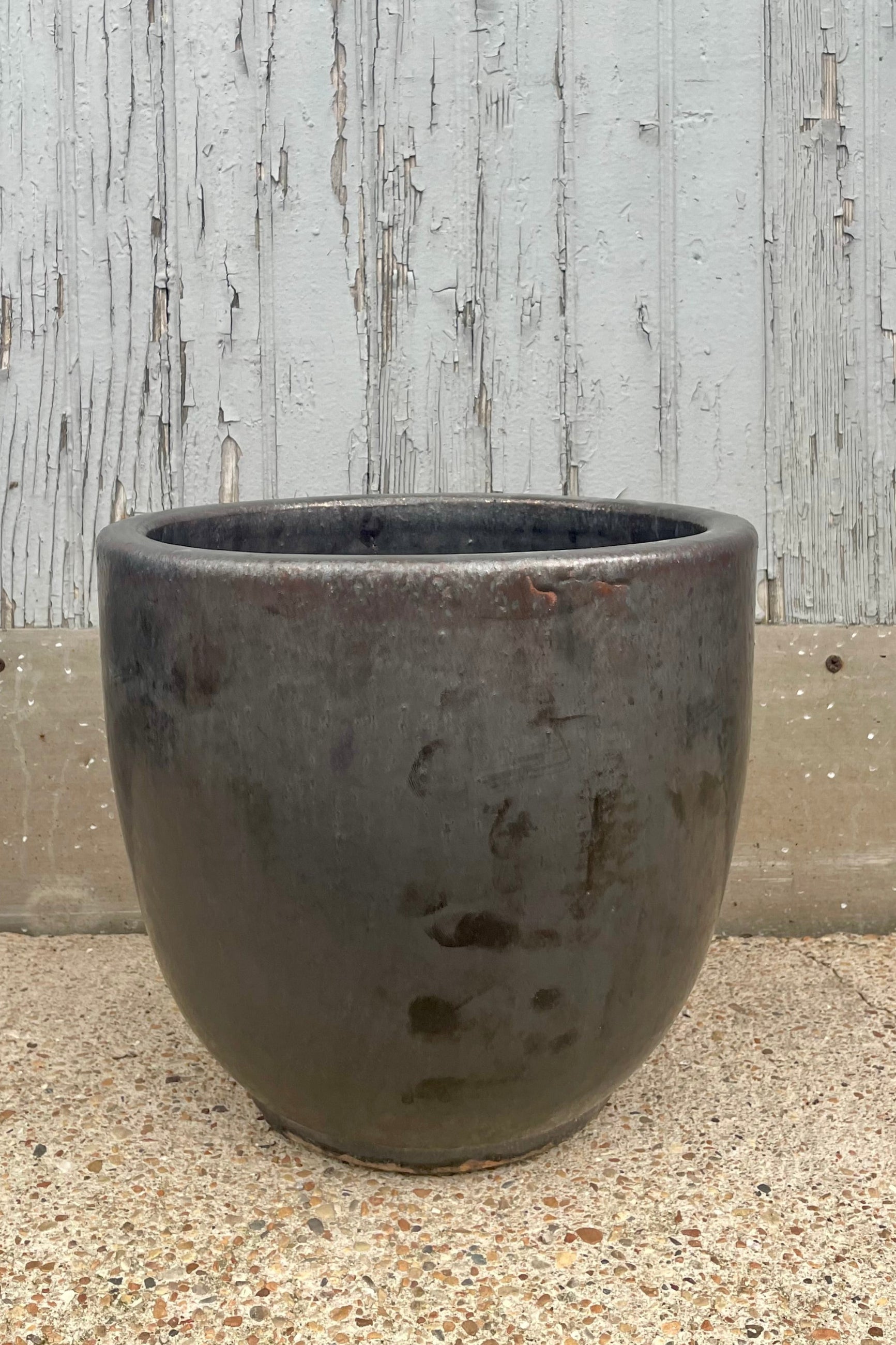 A dark gray or black pot in front of a wooden wall shown from the front ©Sprout Home