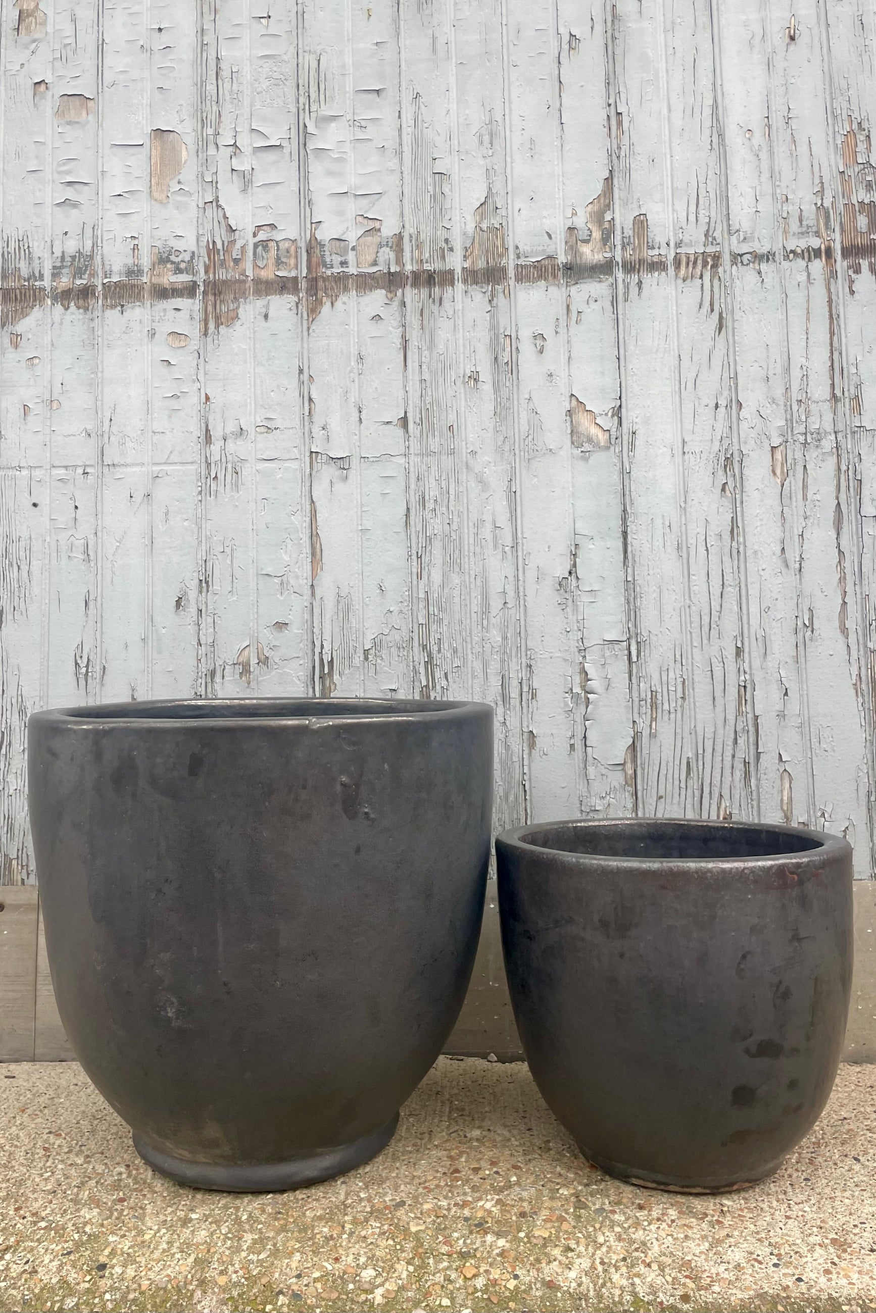 Two dark gray planters are shown in front of a wooden wall. They are two different sizes. Shown from the front ©Sprout Home