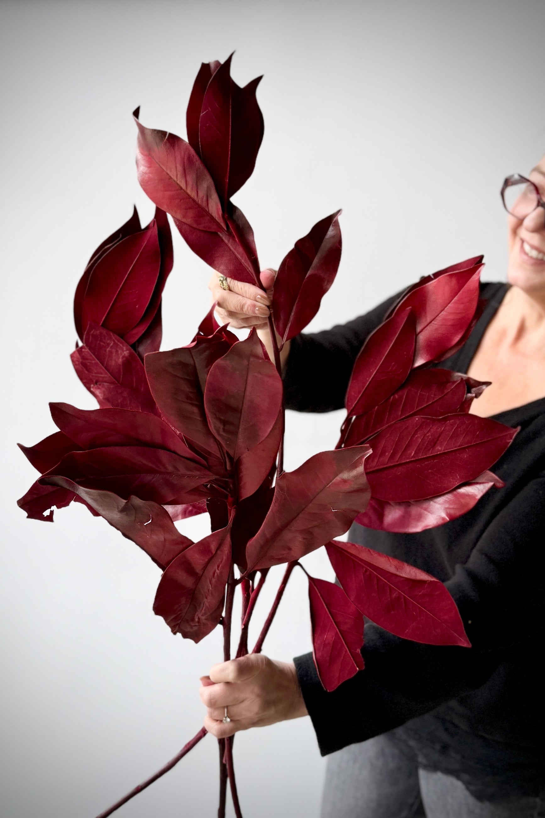 Person holding a bouquet of red preserved Magnolia leaves against a plain background ©Sprout Home