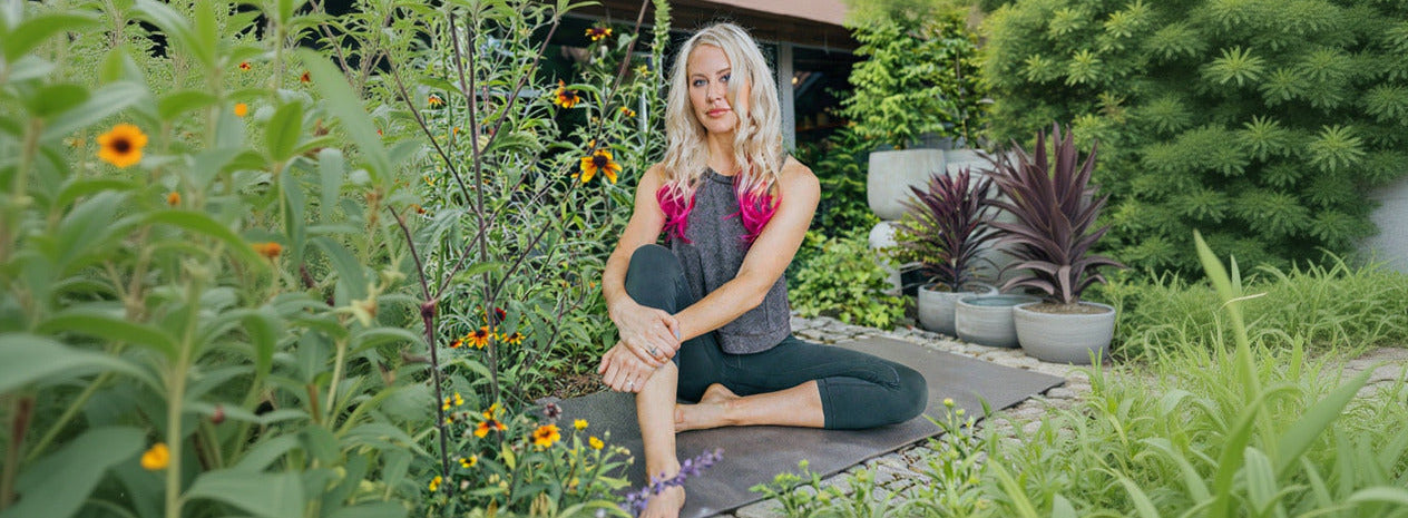 Woman sitting on a mat in a garden with flowers and plants around her. ©Sprout Home