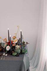 Mo & Co Charcoal beeswax taper candles shown lit and in a table setting with fruit and flowers. 