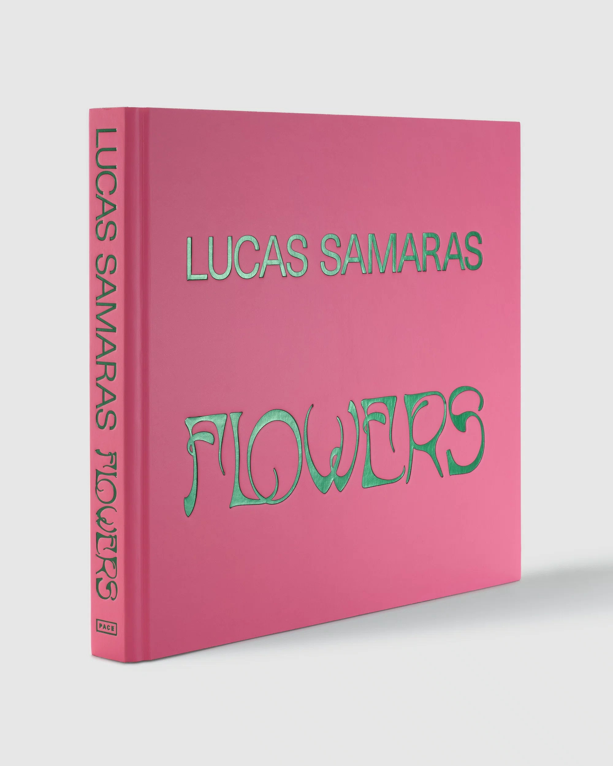 Lucas Samaras 'Flowers' art book shown at a three-quarter angle on a light gray background. The book cover is a vibrant pink with the title 'FLOWERS' in a stylized metallic green font and the artist's name 'LUCAS SAMARAS' in a clean metallic green font on the front cover and spine. ©Pace Publishing