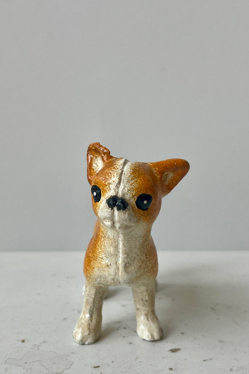 Photo of a white and tan Chihuahua figurine looking toward the viewer. It is shown on a white surface against a white wall.