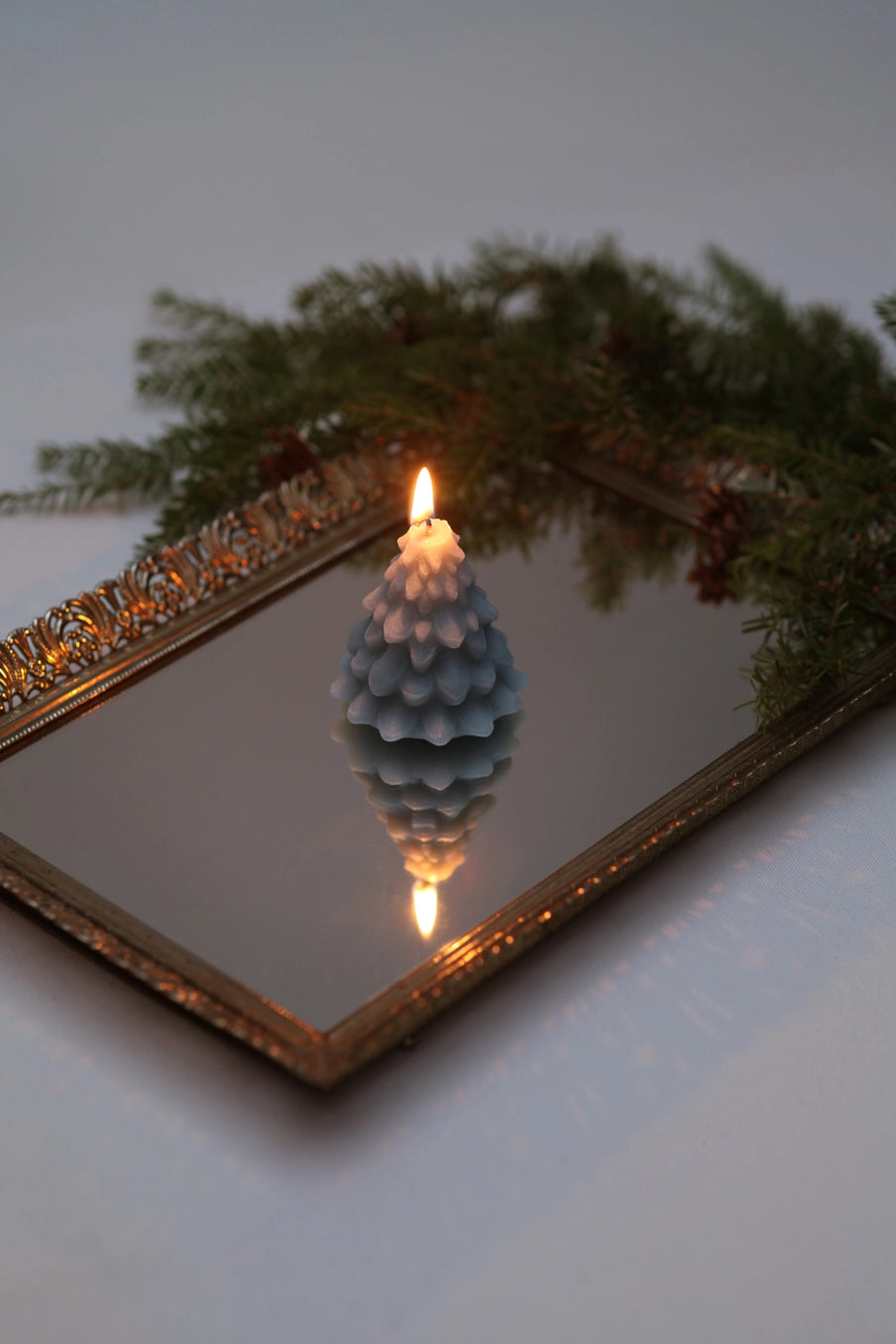 Fir cone-shaped candle on a mirror with decorative greenery ©Mo&Co.