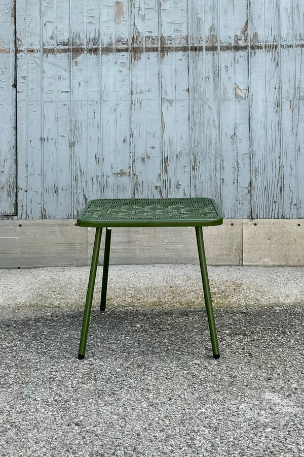 The green Martini 18" side table in front of a gray blue wood wall.