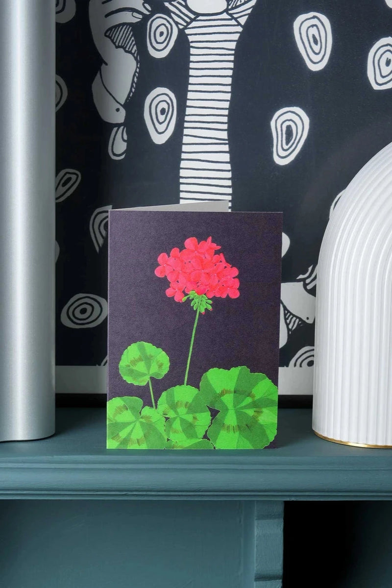 Barbican Geranium Greeting Card by Stengun Drawings on a shelf with black and white wall paper behind it.