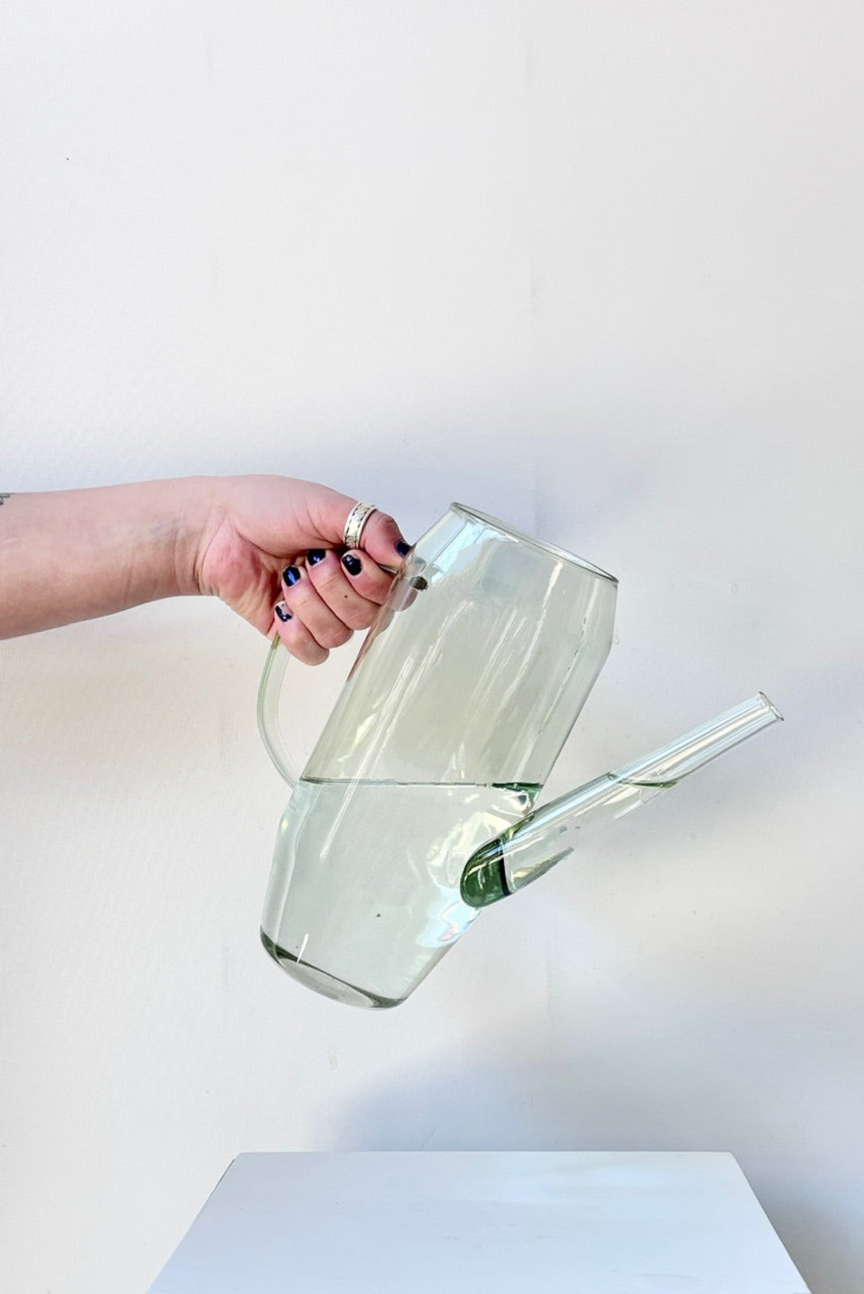 Hand holding clear glass Foray watering can against a white background ©Sprout Home 
