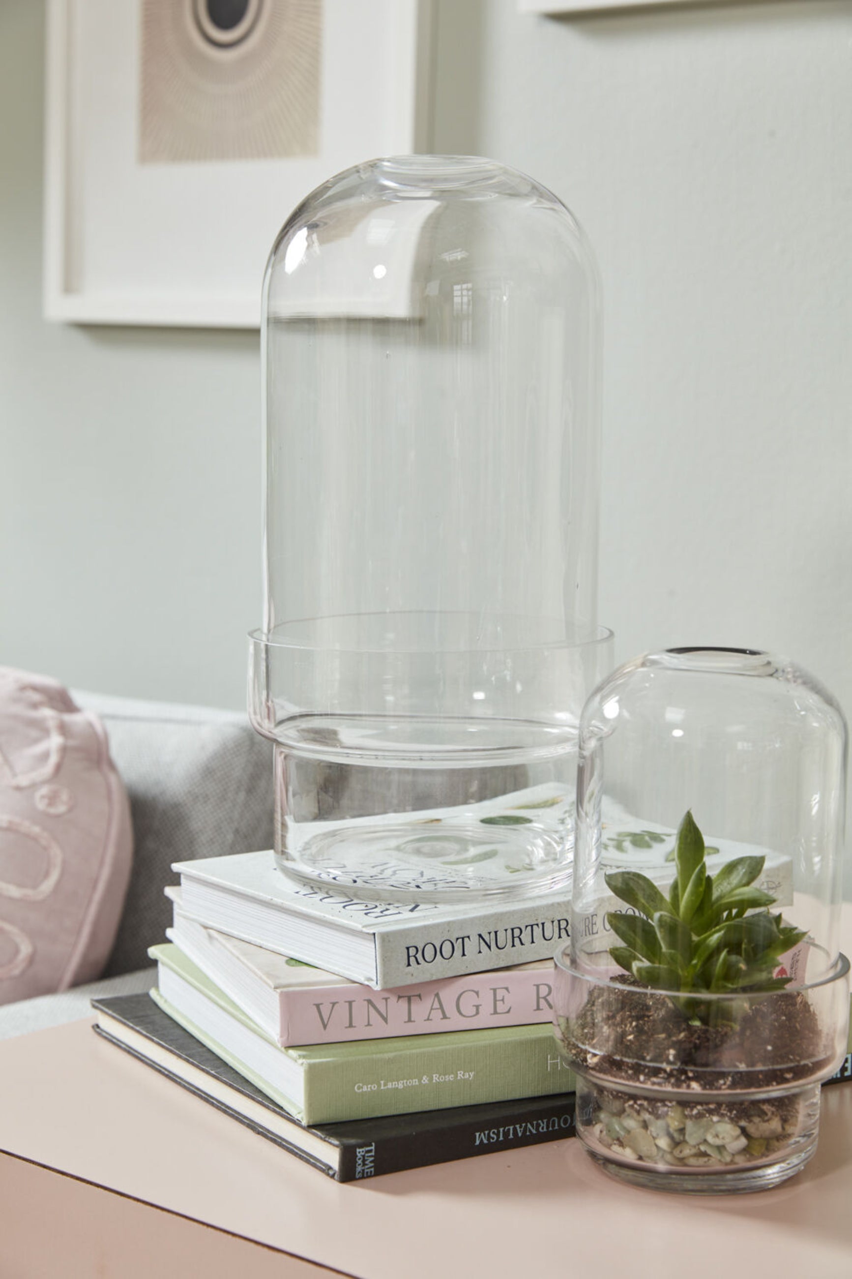 Two different sized Griffith terrariums with the smaller one planted and sitting on a side table with books.