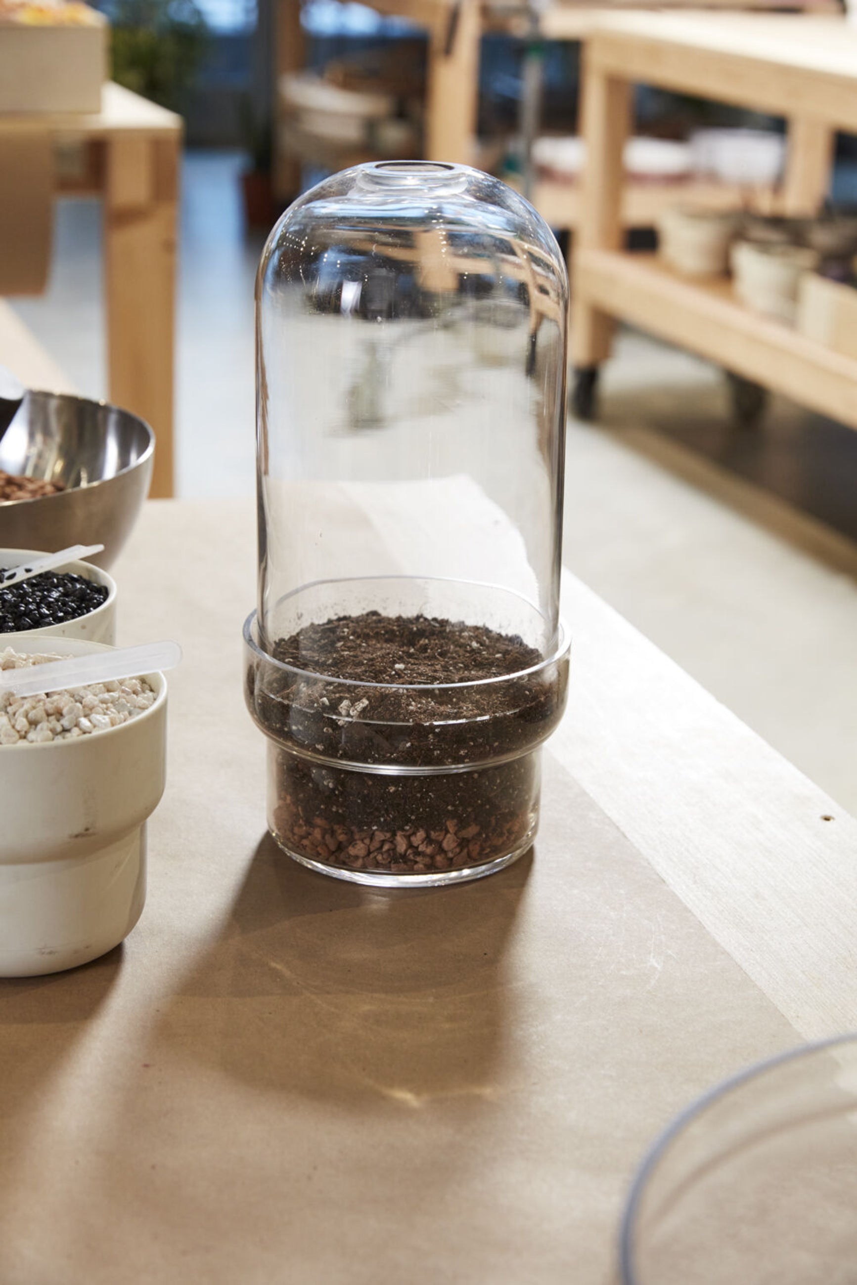 A griffith terrarium in the beginning stages of being planted with dirt and bottom drainage with no plants and sitting on a wooden workbench