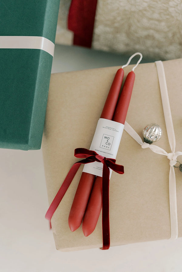 Mo & Co berry red beeswax candles  with a red velvet bow on top of presents.