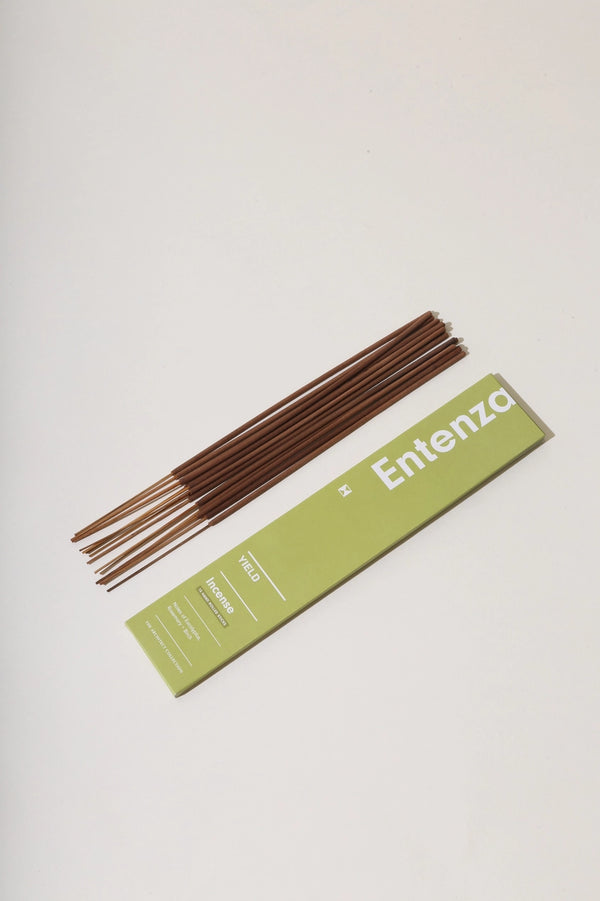 Entente Stick Incense by Yield with its green packaging and sticks sitting next to it. 