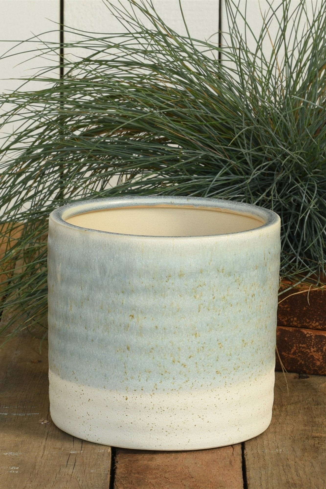 Isle Ceramic cachepot in blue by Homart empty and with a green grass like plant behind it.