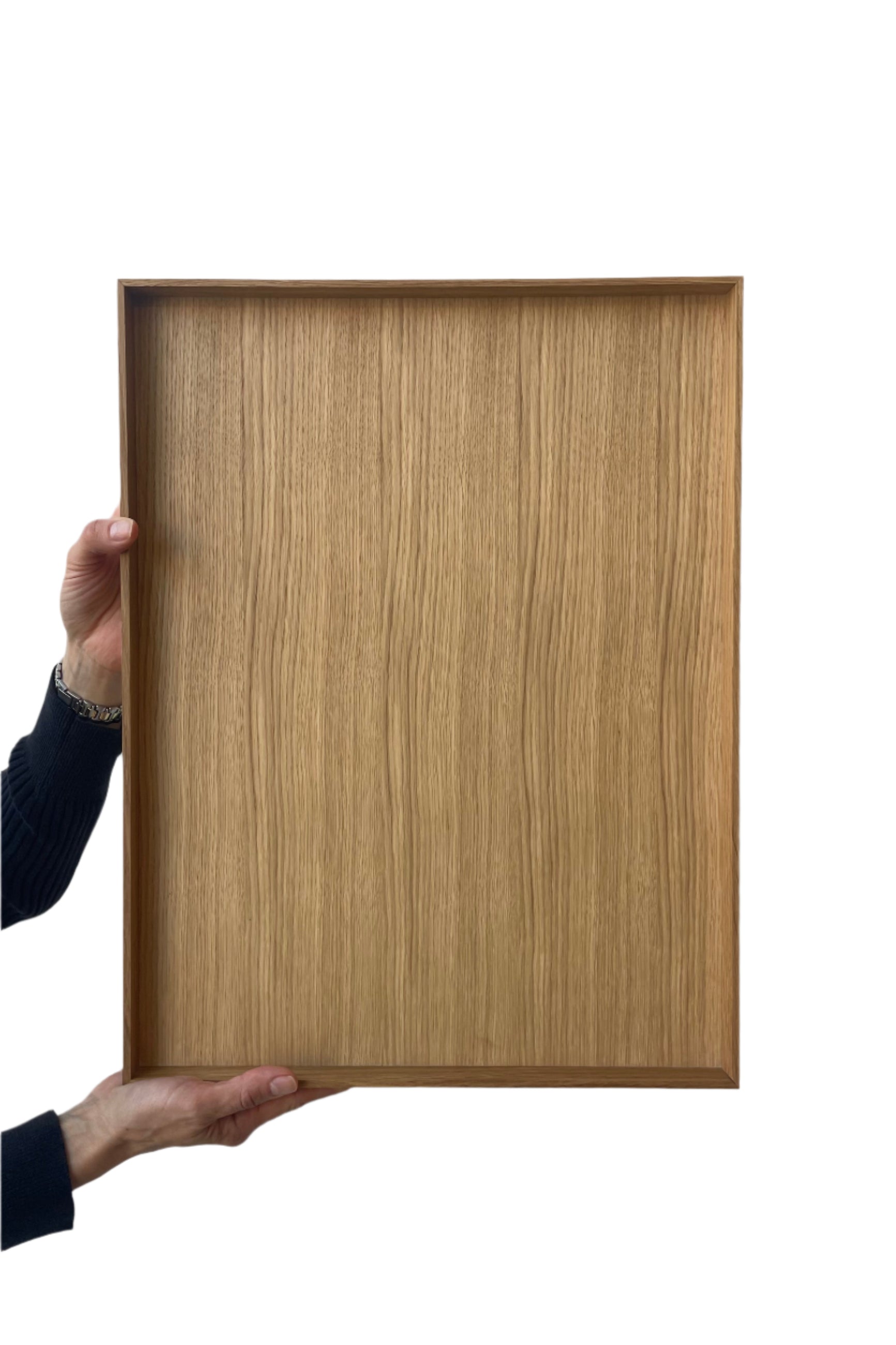 Photo of hands holding a Ferm Living Bon Wooden Tray facing the viewer. The woodgrain of the surface of the tray is visible. Shown in front of a white wall ©Sprout Home