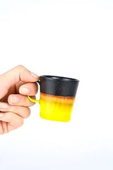 Black & Golden Glaze espresso cup by SGW labs being held by a hand against white