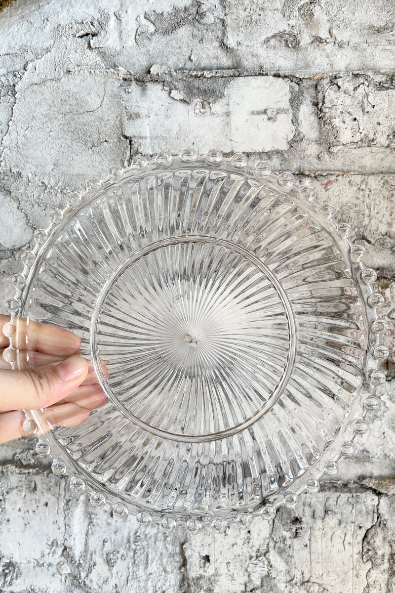 clear dentelle aurora glass plate being held against a white brick wall.