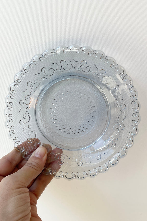 Dentelle Aquamarine Chantilly glass plate hand held against a white wall.