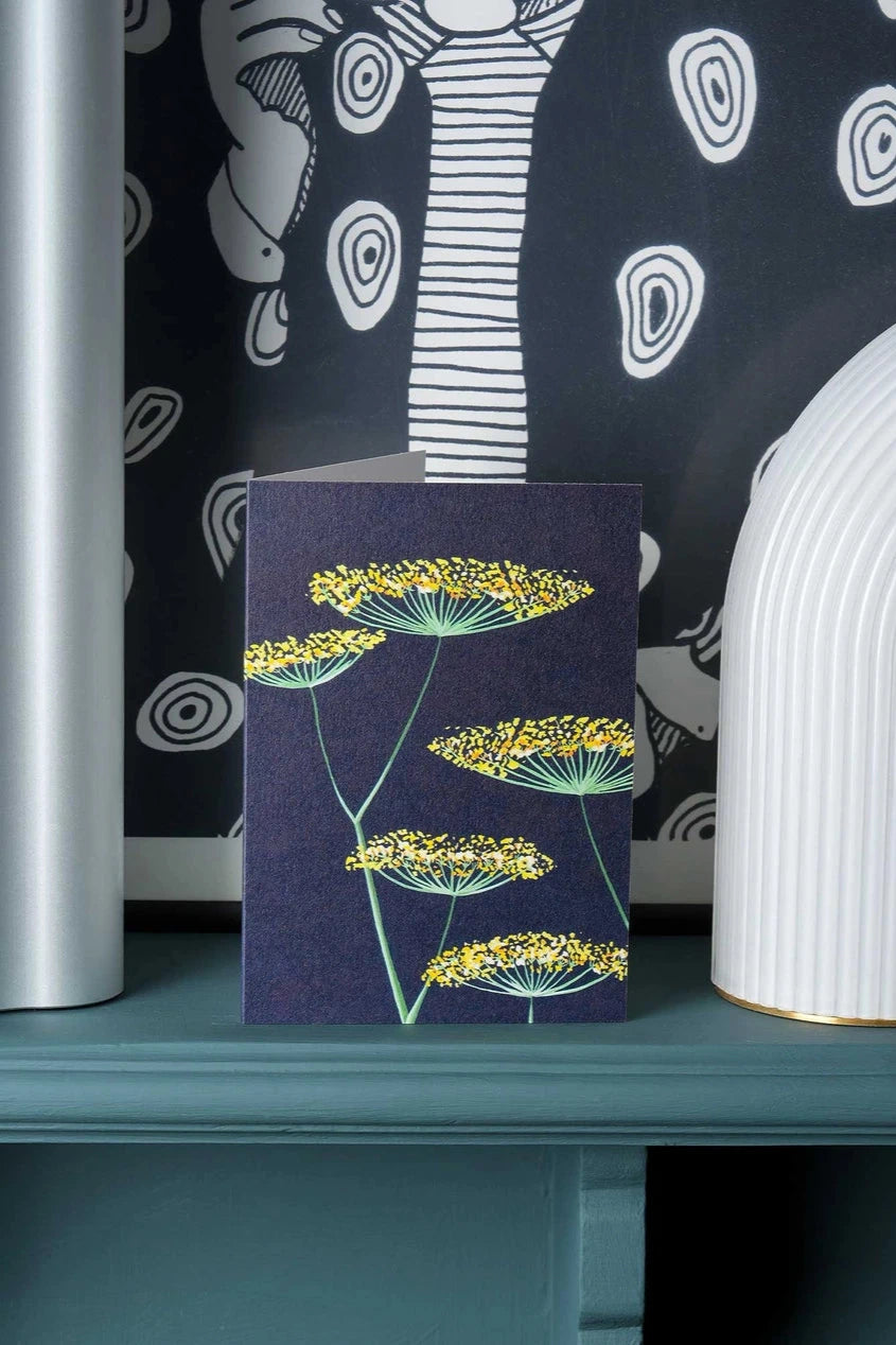 Fennel on Navy card by Stengun Drawings  in a lifestyle shot with it sitting on a ledge with graphic black and white wallpaper behind.