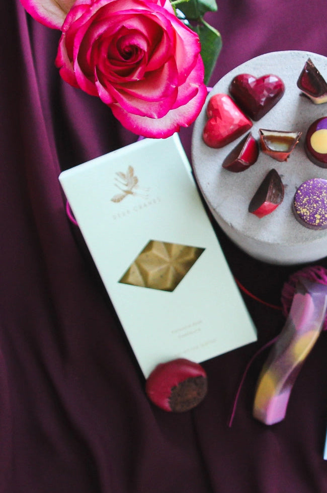 Assorted chocolates on a white plate with pink roses and gift boxes on a purple fabric background ©Deux Cranes