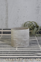 Paso Linear cement cachepot by Homart on a black and white striped cloth with an airplant behind it. 