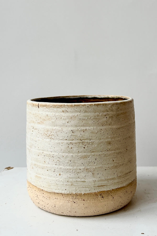 Stoneware ceramic cachepot with a weathered, beige, raw clay finish and glazed interior against a white background.