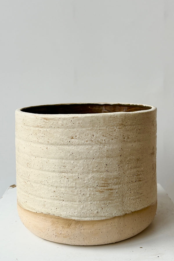 Stoneware ceramic cachepot with a weathered, beige, raw clay finish and glazed brown interior against a white background.