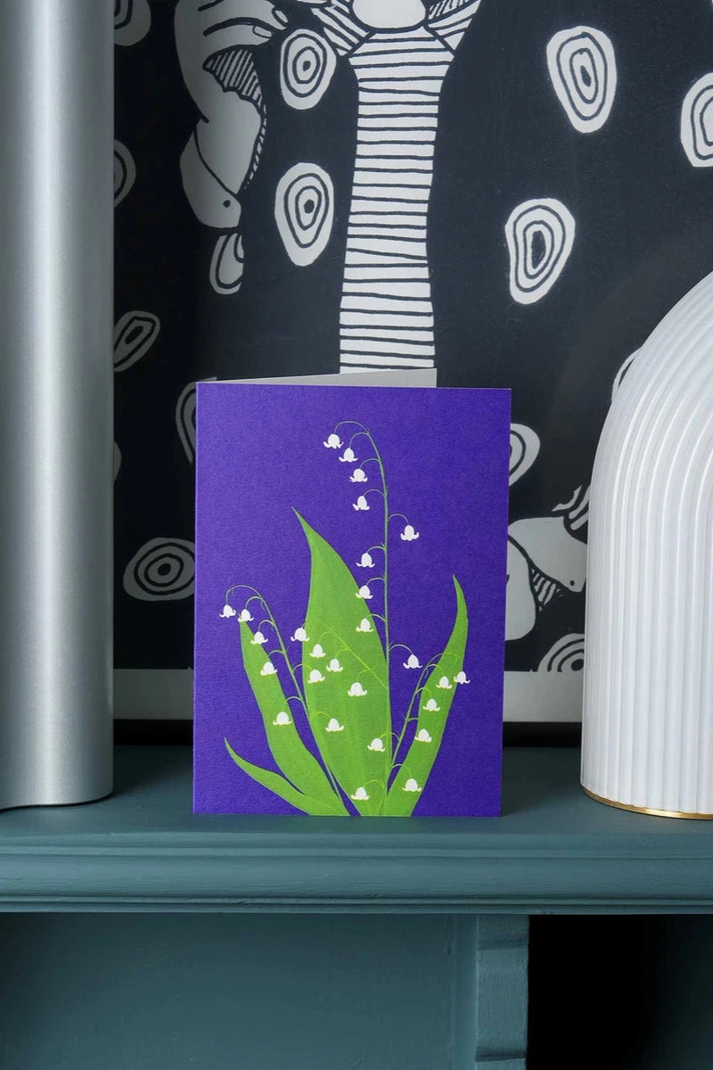 Lilly of the Valley greeting card by Stengun Drawings on a shelf showing off the print blue against black and white wall paper.