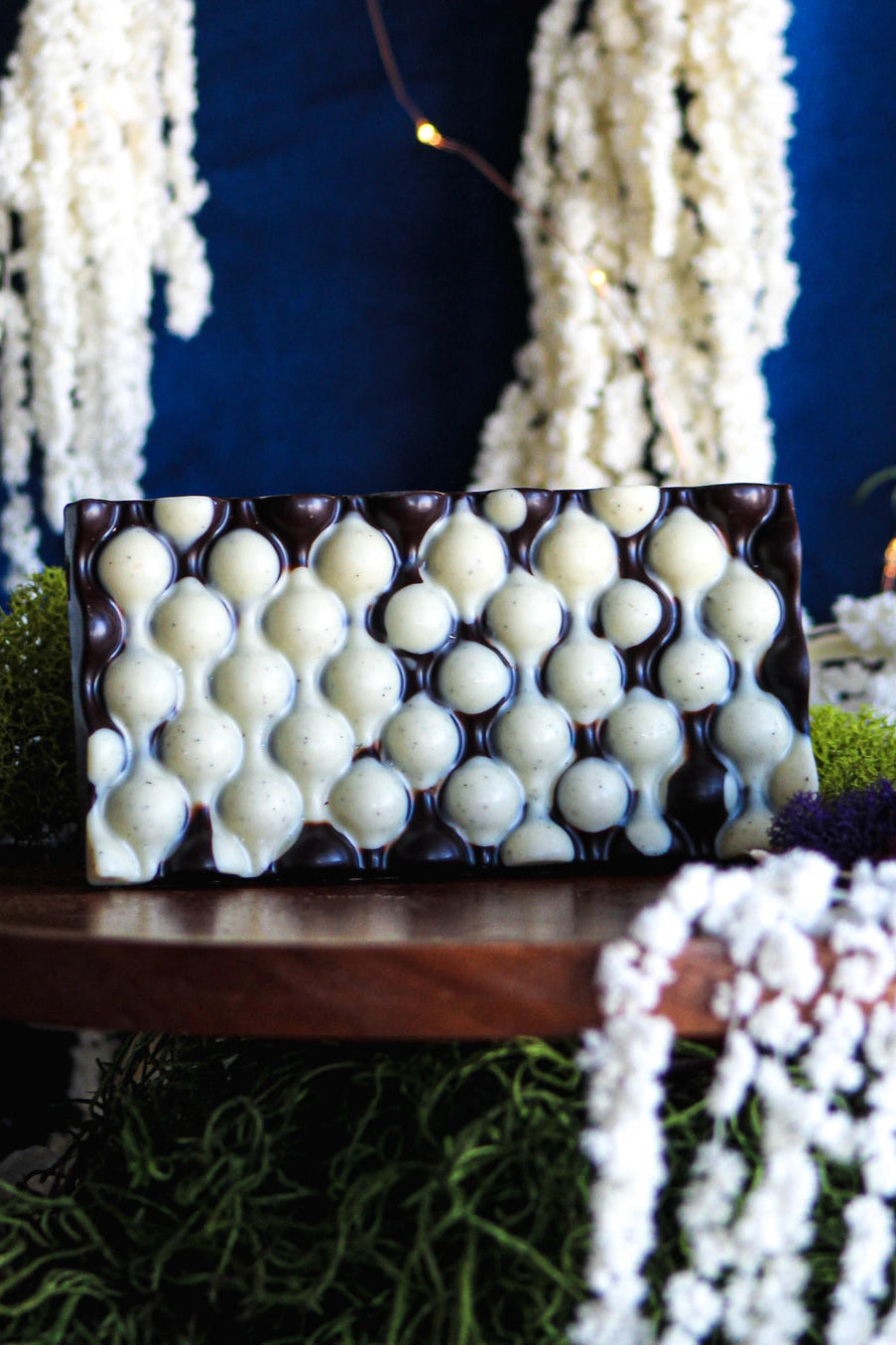 Chocolate bar with a unique pattern on a wooden stand surrounded by decorative elements. ©Deux Cranes