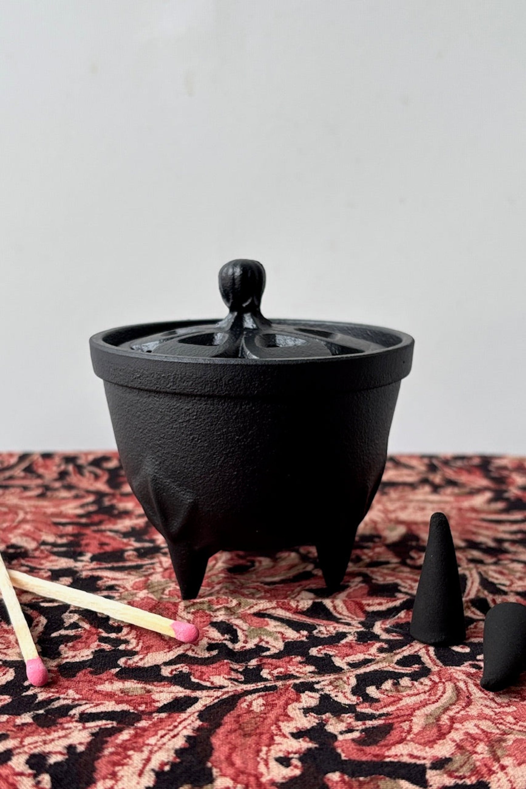 Cast iron incense charger with floral cut out  lid on a decorative tablecloth with incense cones ©Sprout Home