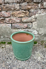 View from above. Photo of I/O2 sea green planter and saucer from the side. The semi-gloss glazed pot sits atop a fitted saucer. The photo is taken in front of a brick wall.