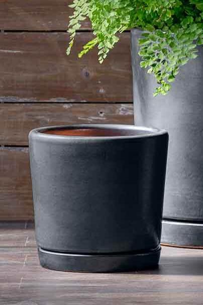 Small I/O 2 Graphite glazed pot with a saucer against a wood slatted wall